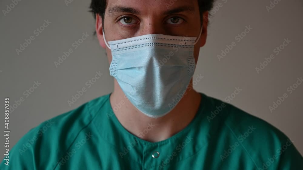 young male nurse or doctor with mask raising his head and looking at the camera young male nurse or doctor with mask raising his head and looking at the camera