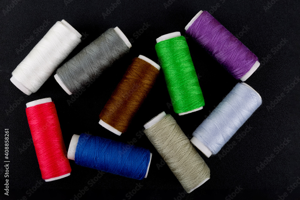 Multicolored threads on a black background.Sewing Spools of thread. White, gray, blue, purple, brown green, red colors.Selective focus.Top view.Flat lay.Сoncept of hobby,sewing,decoration. Multicolored threads on a black background.Sewing Spools of thread. White, gray, blue, purple, brown green, red colors.Selective focus.Top view.Flat lay.Сoncept of hobby,sewing,decoration.