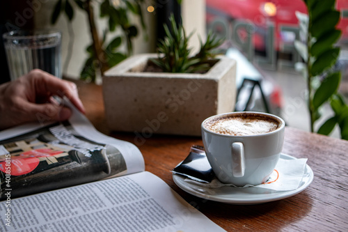 Hand of a person leafing through the newspapers or a magazine, with a cup of coffee in front of a cafe window. 