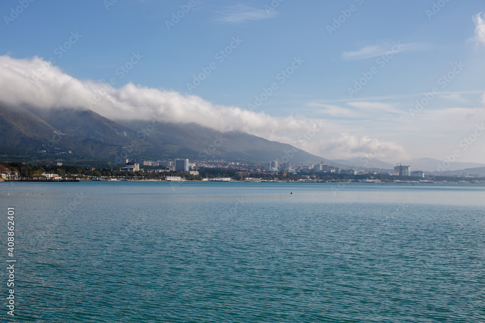 A white cloud lies on a mountain against the background of the sea
