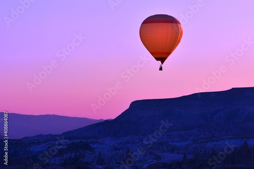 Beautiful Red hot air balloon flying over the valley Cappadocia at pink sunset. Launching a colorful hot air balloon in the mountains of Cappadocia on purple sky