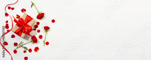Long wide greeting banner for St. Valentine’s day with gift box, beautiful red roses and ribbon on white marble background. St. Valentine’s promo and sale banner concept. © Iryna