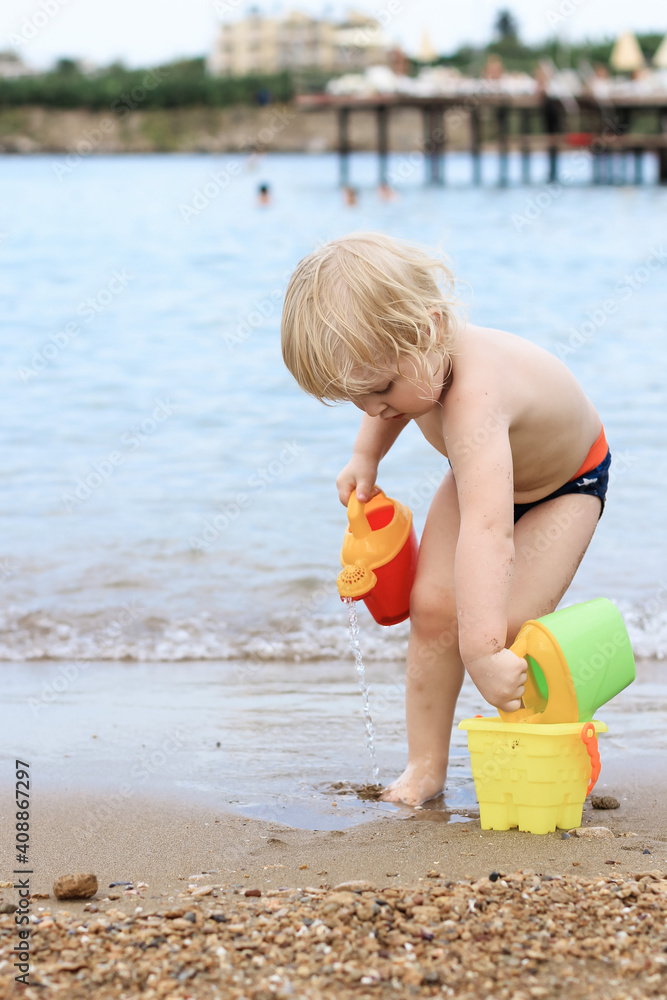 Little boy playing on the beach with plastic toys. Summertime, vacation, travel, childhood concept. Little boy playing on the beach with plastic toys. Summertime, vacation, travel, childhood concept.
