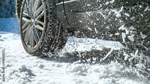Fotografie CLOSE UP: Powerful car's wheels spin in place and spew up pieces of white snow