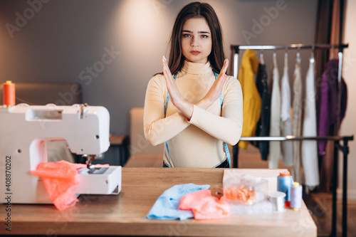 Young dressmaker woman sews clothes on sewing machine. Seamstress in workshop shows what not allowed to do. Creating online clothing design courses.