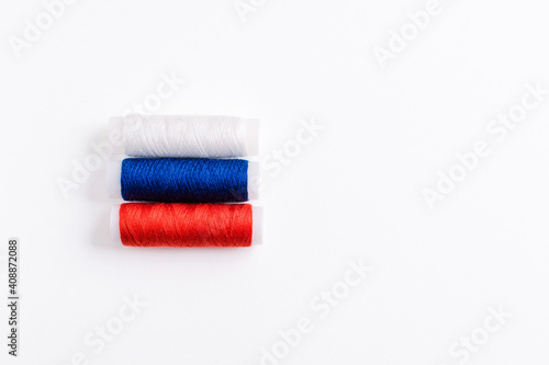 Three spools of thread for sewing are stacked in the form of the flag of Russia on a white background. Concept of Russian patriotism and the country's clothing industry. There is a free empty space.