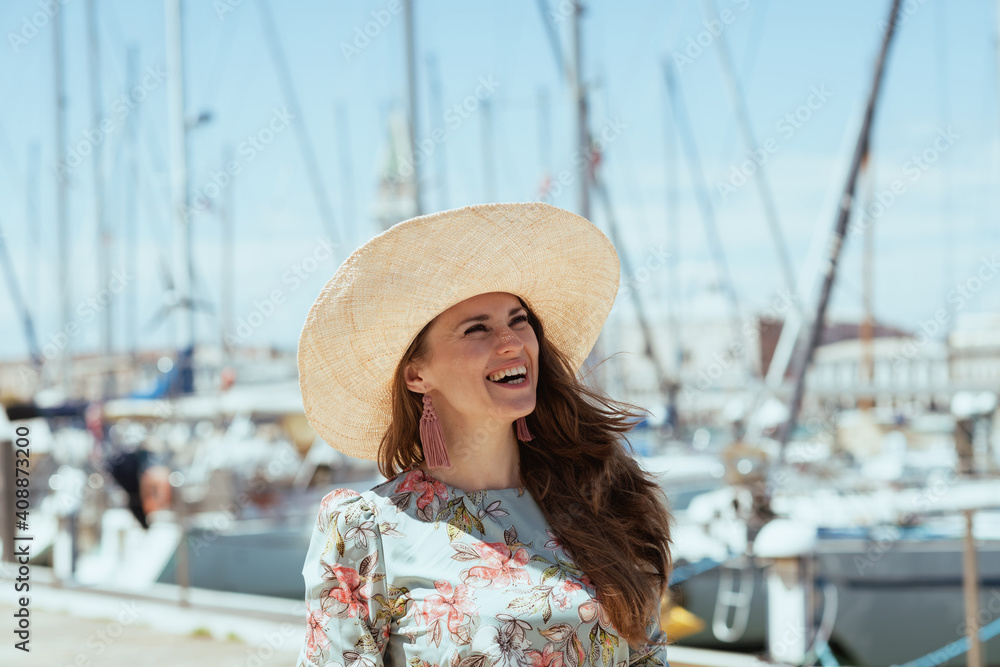 smiling stylish solo traveller woman in floral dress on pier