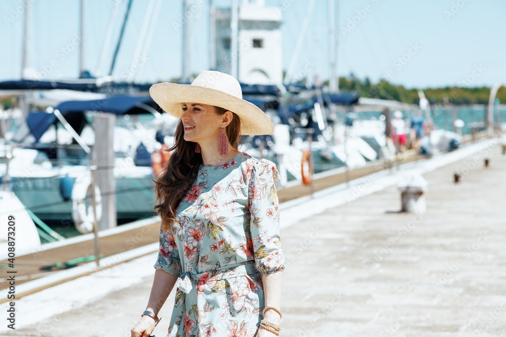smiling trendy traveller woman in floral dress on pier