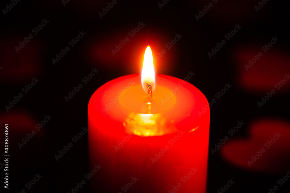 red burning candle on a black background, scattered around red hearts