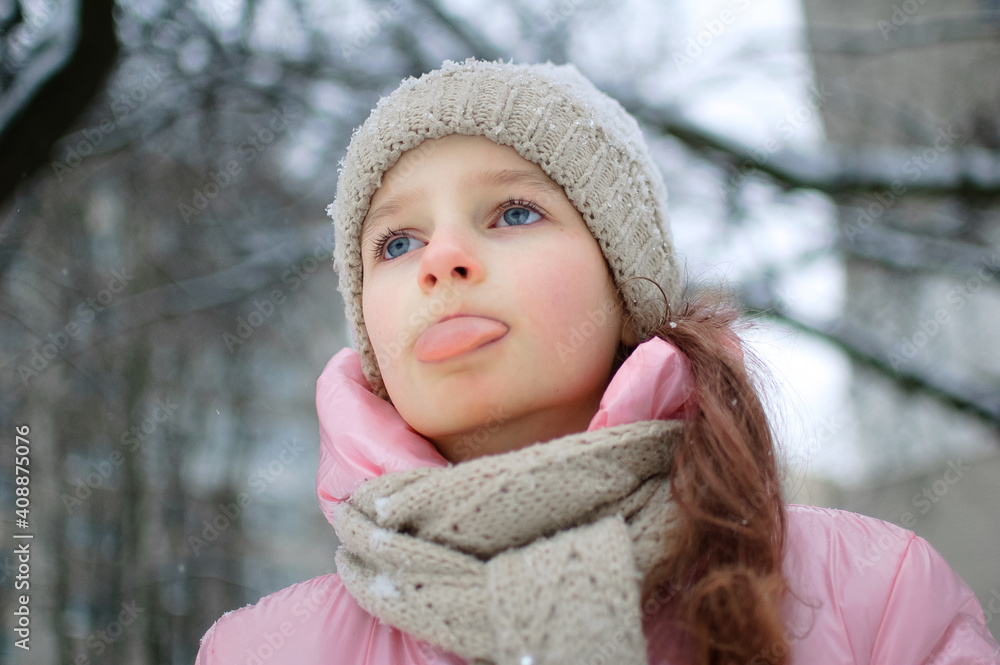 A girl playing with snow in winter, eating snow with tongue and closed eyes outdoors in winter clothes. Happy childhood and active holidays. A girl playing with snow in winter, eating snow with tongue and closed eyes outdoors in winter clothes. Happy childhood and active holidays.