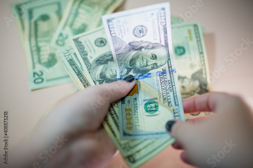 Close-up of a hand holding a pile of US banknotes. Cash of one hundred dollar bills. Background of many banknotes