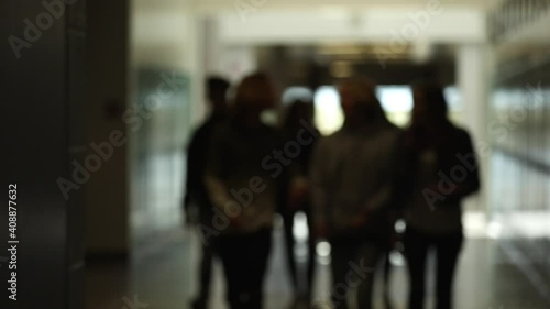 Out of focus view of students walking in school hallway in small group of friends.