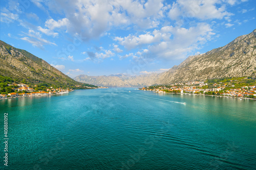 A motor boat glides down the Boka Bay near the ancient hillside towns of Perast and Kotor, with the mountains of Montenegro in the distance.