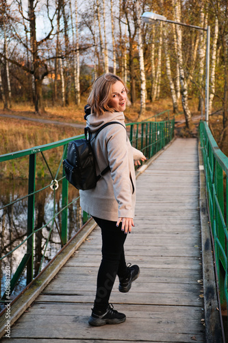 Portrait of attractive woman goes and fooling around on the bridge over the river in autumn park. Authentic people.
