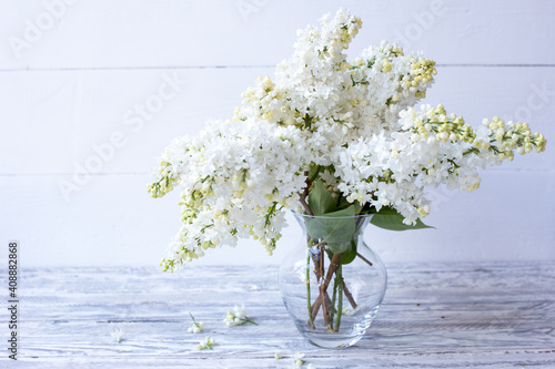 White lilac bouquet in glass vase on wooden table. Spring branches of blooming lilac festive bouquet of flowers with copy space.
