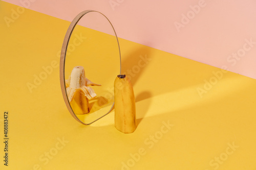 Half of banana in a mirror with one half pilled off. Dual tone background.  Creative fruit concept