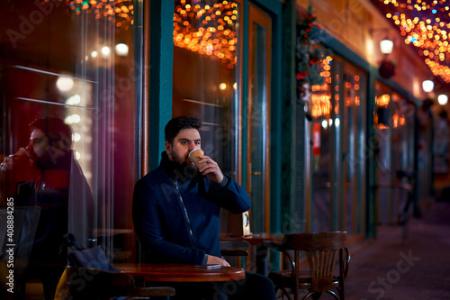 young adult man sitting alone in urban outdoor cafe on the night cozy narrow street