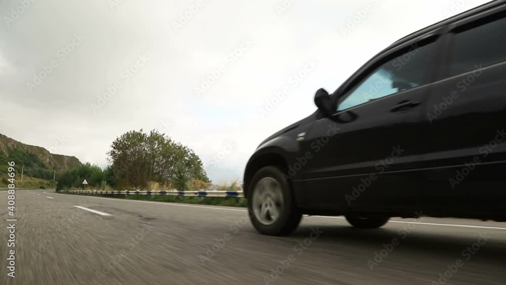 The car drives along a flat asphalt road between the lake and green hills with forests. The car drives along a flat asphalt road between the lake and green hills with forests.