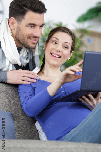 happy pregnant couple slooking on laptop sat on a couch