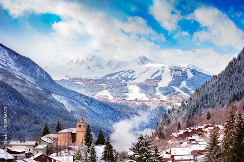 Panorama of Champagny-en-Vanoise village with mist and clouds around old church  over Courchevel resort on background
