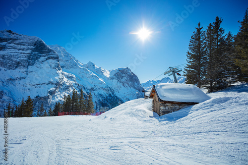 Small covered with snow house and mountain peaks over clean empty ski trails in French Alps photo