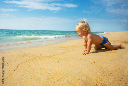 Portrait of happy little toddler boy crawl on the beach towards the sea