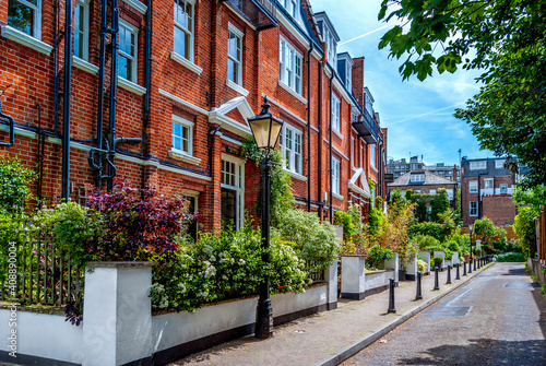 Residential street with red-brick houses and bushes of colorful flowers in Hampstead area, north London, England. 