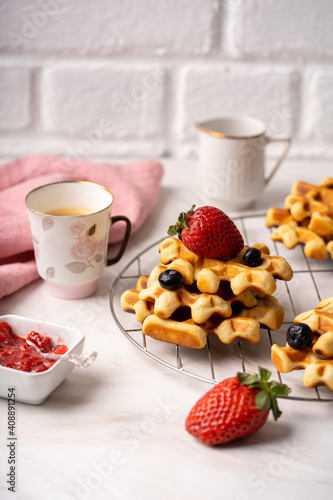 Delicious breakfast table, waffles with berries, jam and cup of coffee. Front view. High quality photo