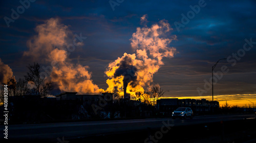 Silhouette landscape industrial factory with dark toxic smoke explodes in the air, over the golden sunset sky. Dramatic scene of bad environment, pollution and global warming. Save the world concept.
