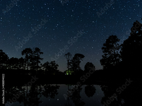 night sky with trees and stars reflecting on a pond