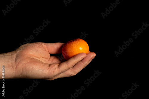 Hand holding ripe tangerine on black isolated background