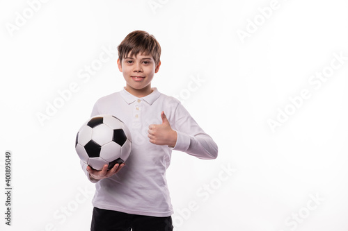 A happy young boy holding a soccer ball is showing a thumb up at the camera © Sergiu
