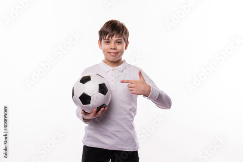 A nice picture of a boy holding a soccer ball and smiling at the camera is pointing at it