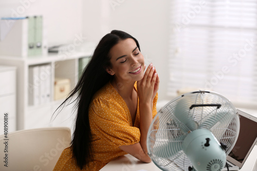 Valokuva Young woman enjoying air flow from fan at workplace