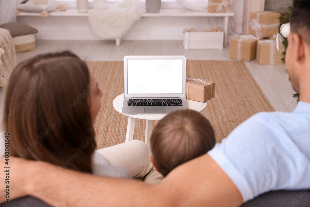 Family with child using video chat on laptop in room decorated for Christmas, back view Family with child using video chat on laptop in room decorated for Christmas, back view