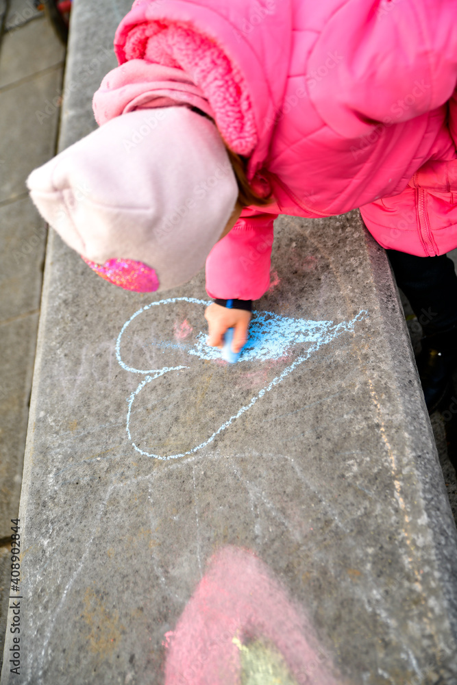a girl in a pink jacket draws hearts with crayons on a large concrete bench