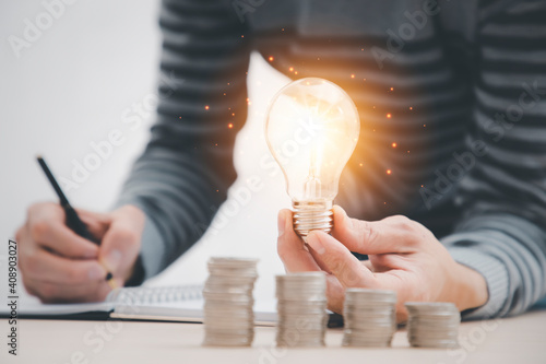 businessman hand holding light bulb with coins stacking on desk.saving energy and money,The idea of ​​inspiration from online technology.innovation idea concept.
