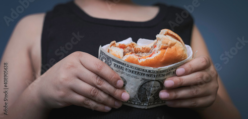 Niño sosteniendo co sus manos una hamburguesa cubierta con una billete de dólar.