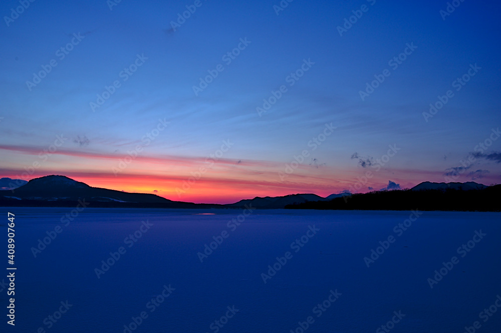 氷った真冬の湖の夜明け。薄明の下の結氷した湖。日の出前の空のグラデーション。屈斜路湖、北海道、日本。