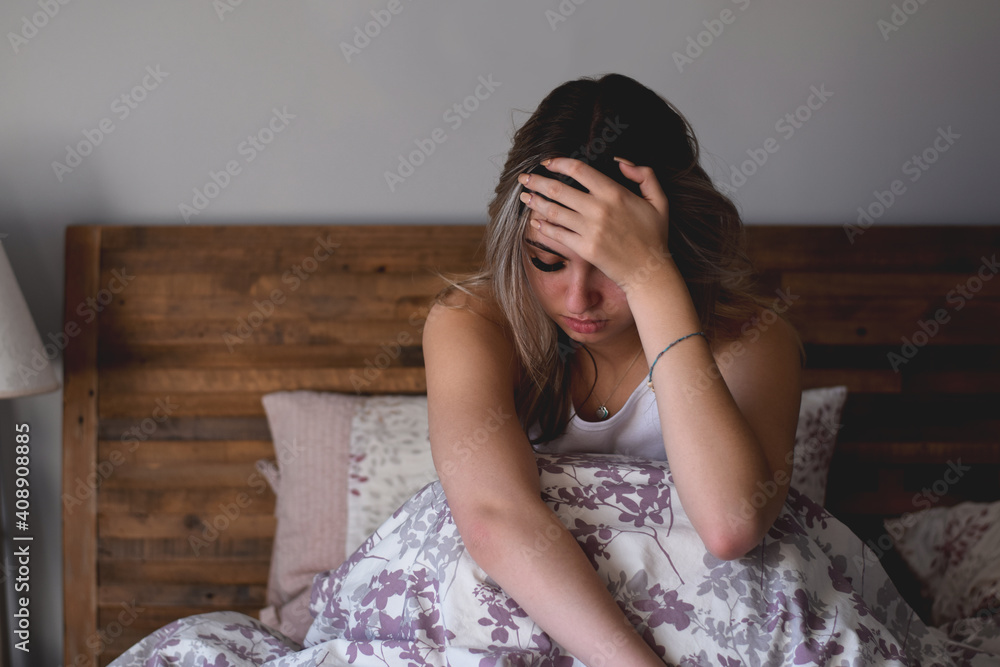 Young teenage girl sitting in bed stressed and upset