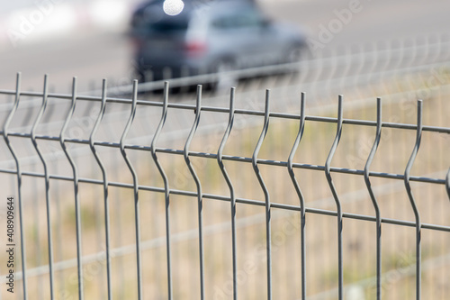 Fence made of thin gray steel twigs next to the road. Sectional metal fencing. Close-up. Selective focus