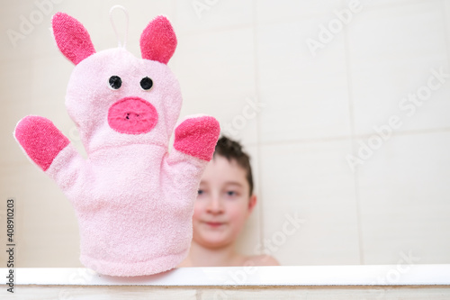 A boy in a bathroom showing funny piggy hand puppet toy washcloth close up, happy washing and shower concept photo