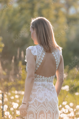 Girl in a white dress in a field with dandelions at sunset