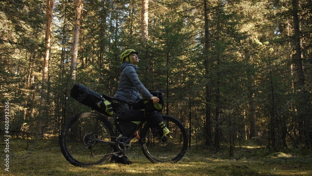 The woman travel on mixed terrain cycle touring with bike bikepacking outdoor. The traveler journey with bicycle bags. Stylish bikepacking, bike, sportswear in green black colors. Magic forest park.