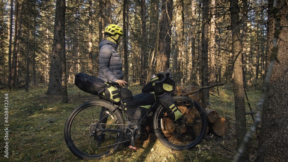 Naklejka premium The woman travel on mixed terrain cycle touring with bike bikepacking outdoor. The traveler journey with bicycle bags. Stylish bikepacking, bike, sportswear in green black colors. Magic forest park.