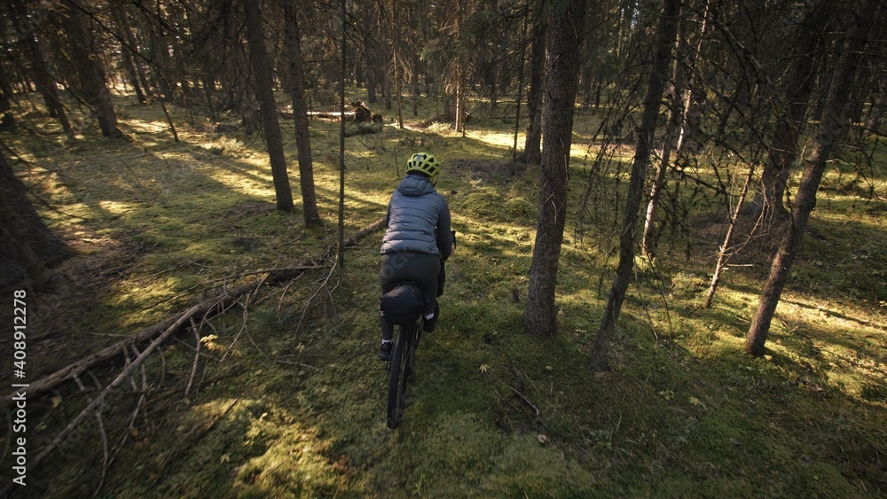Fototapeta premium The woman travel on mixed terrain cycle touring with bike bikepacking outdoor. The traveler journey with bicycle bags. Stylish bikepacking, bike, sportswear in green black colors. Magic forest park.