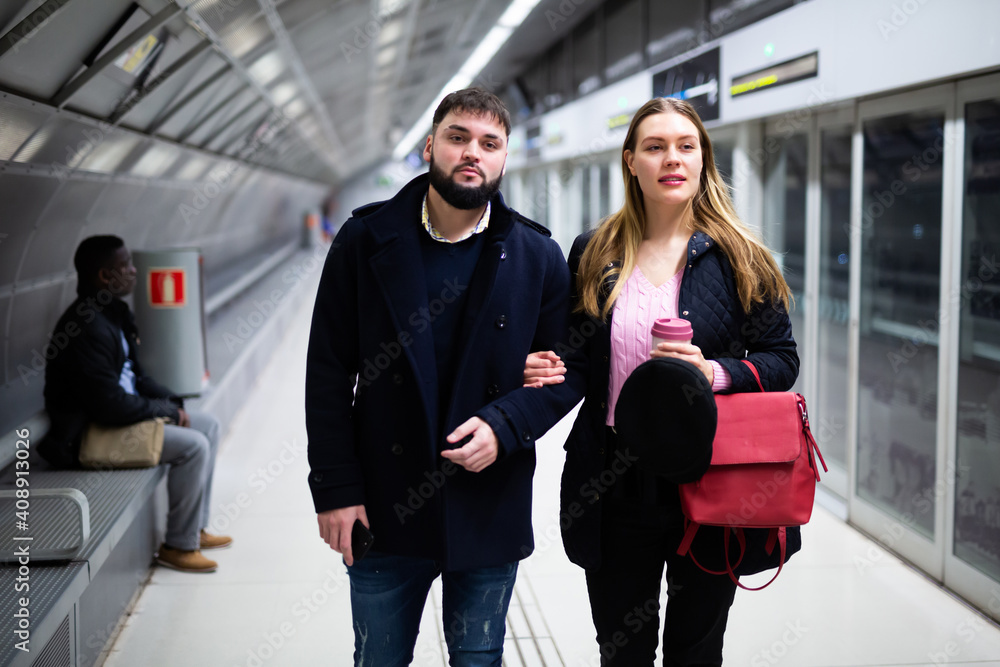 Portrait of couple of young people waiting for subway train, walking at station