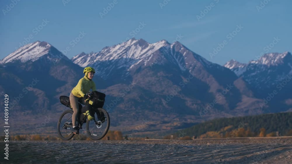 The woman travel on mixed terrain cycle touring with bikepacking. The traveler journey with bicycle bags. Sport tourism bikepacking, bike, sportswear in green black colors. Mountain snow capped. The woman travel on mixed terrain cycle touring with bikepacking. The traveler journey with bicycle bags. Sport tourism bikepacking, bike, sportswear in green black colors. Mountain snow capped.