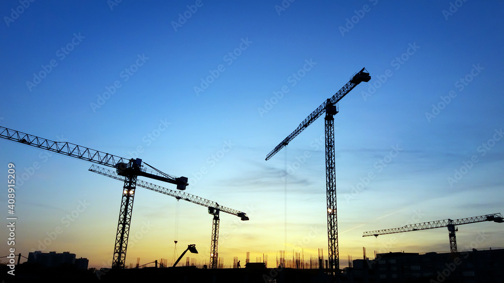 Construction crane silhouettes in blue sky at sunset