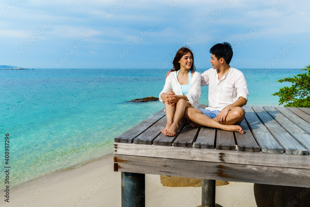 happy young couple sitting on wood bridge and sea beach at Koh MunNork Island, Rayong, Thailand